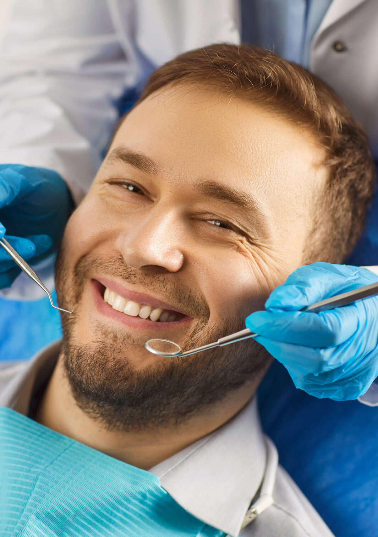 Dental health. Man sits comfortably in dentists chair, showing off white smile that exudes confidence. Dentist holds special tools in his hands for preventive and therapeutic examination of teeth.