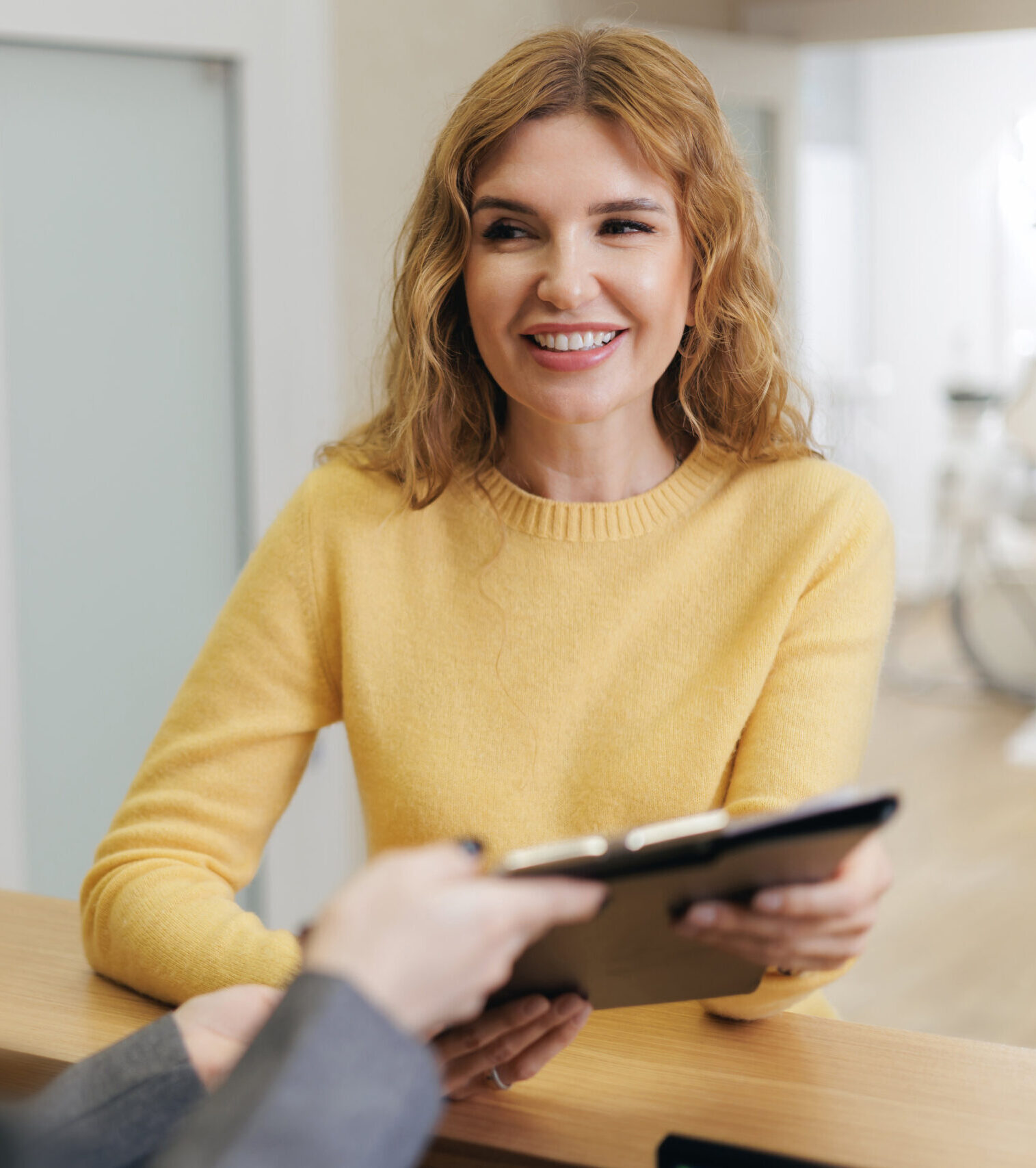 Smiling caucasian female adult with folder for papers at reception desk of clinic.