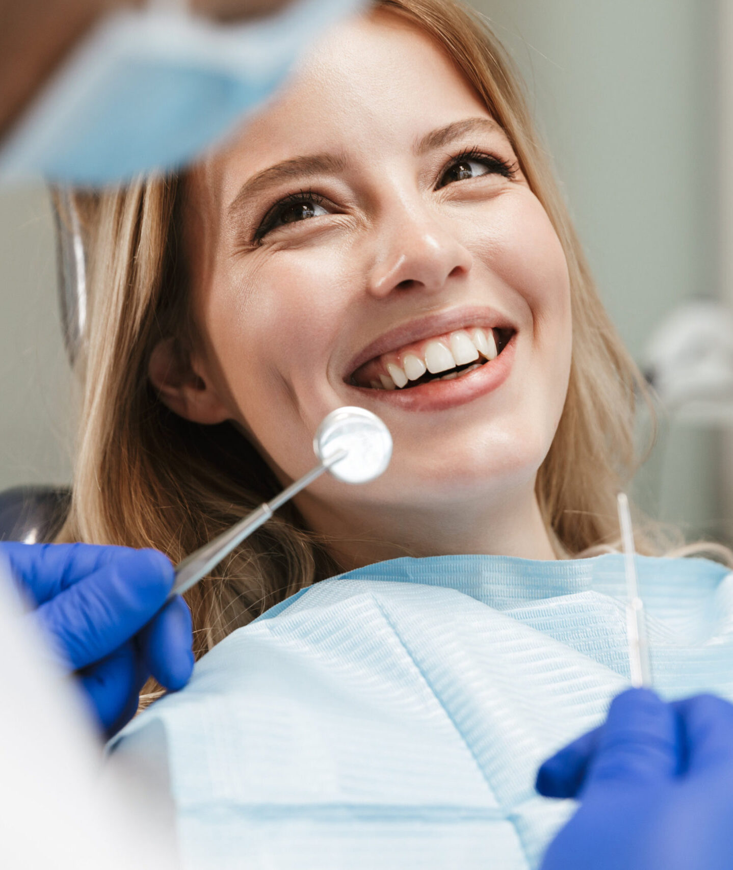Image of pretty young woman sitting in dental chair at medical center while professional doctor fixing her teeth