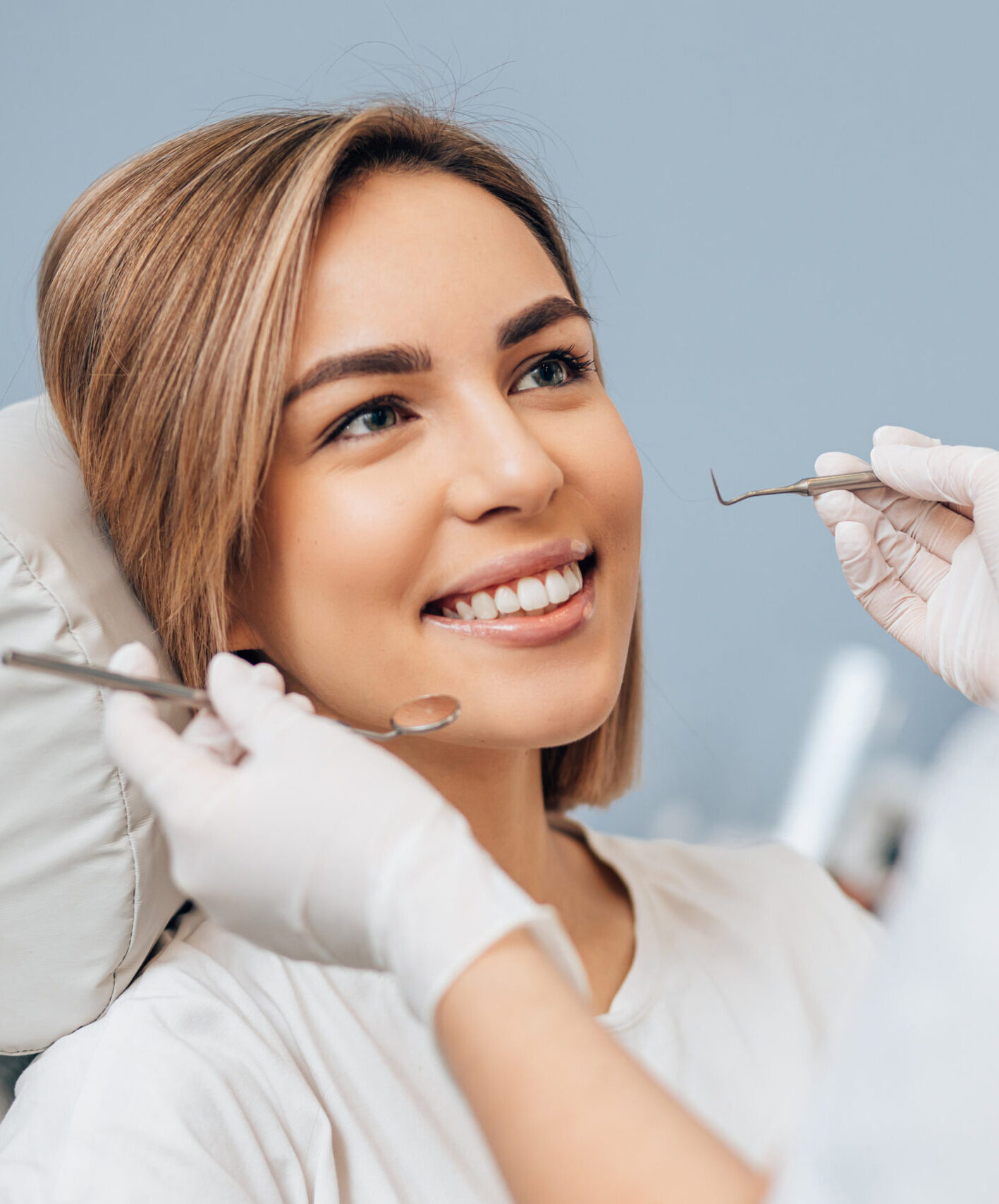 attractive woman with short hair sit in dental office and look at doctor with confidence, she has perfect smile. professional doctor of clinic use special sterilized medical instruments