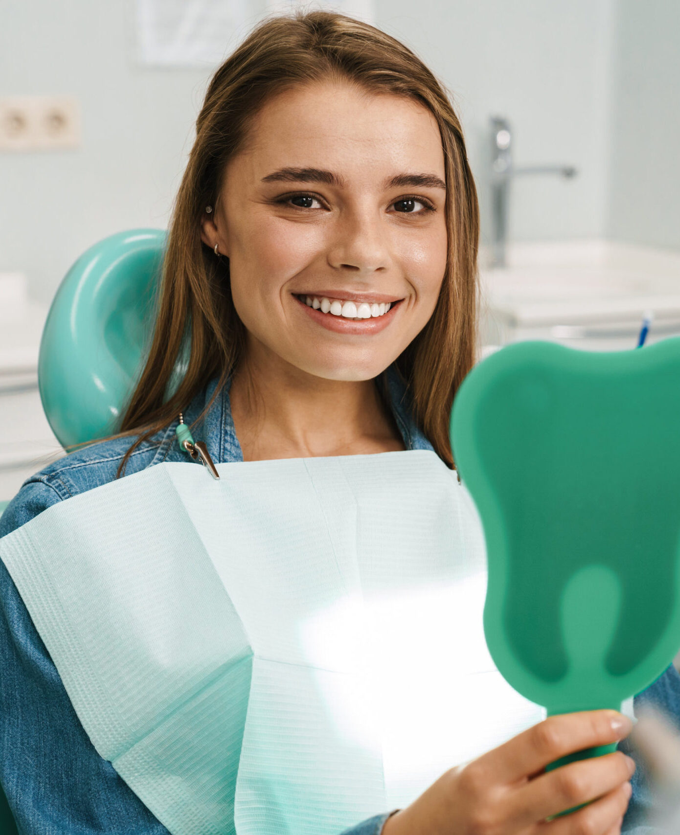European young woman smiling while looking at mirror in dental clinic