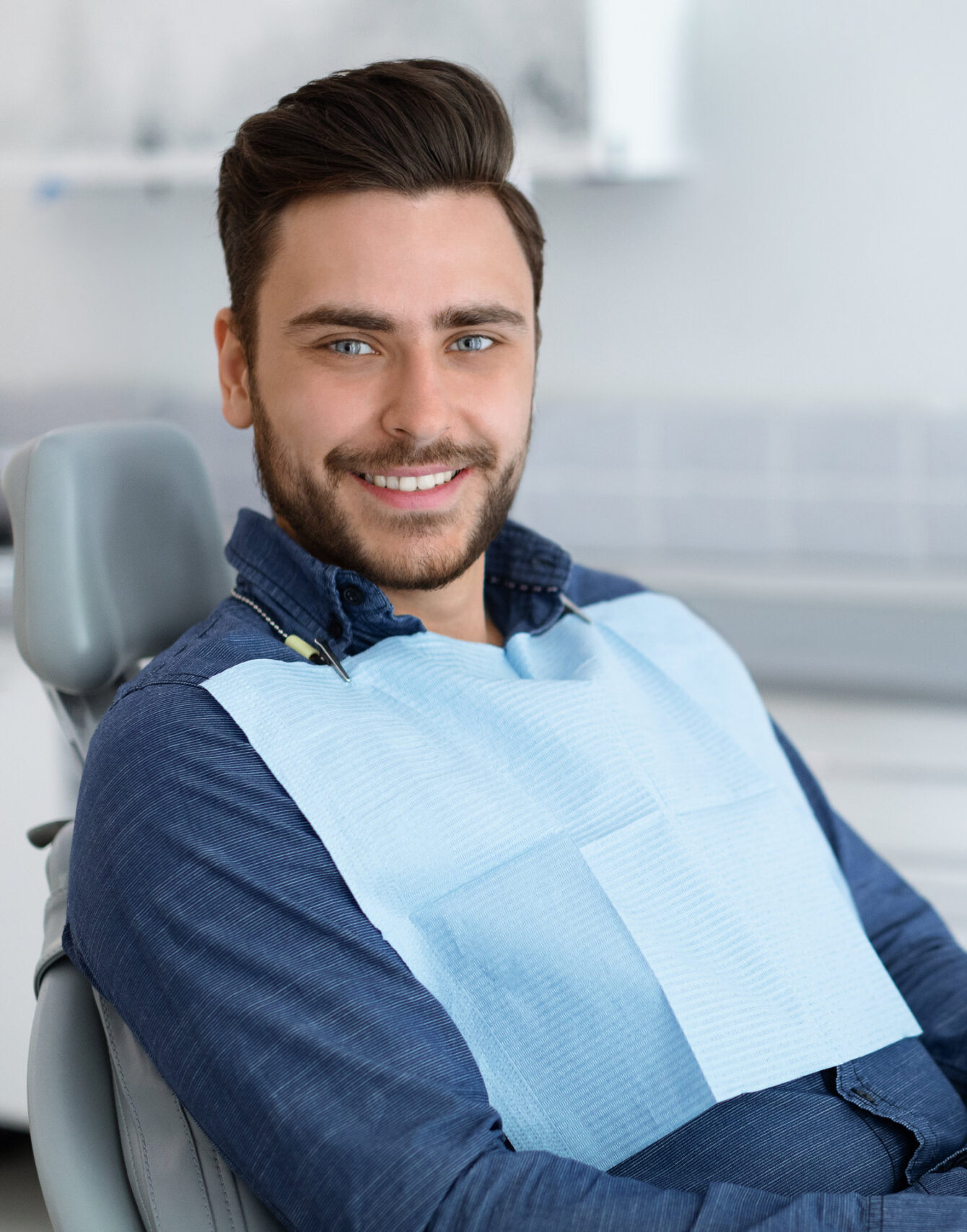 Side view of handsome young man patient sitting in dental chair and smiling, panorama with copy space. Cheerful millennial man showing beautiful white smile after treatment at modern dental clinic