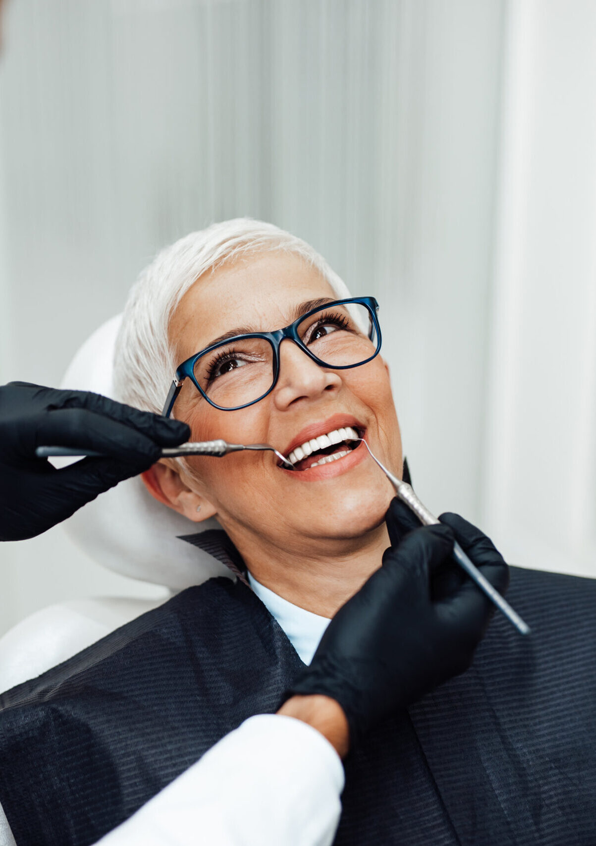 Beautiful senior woman having dental treatment at dentist's office. Dentist is wearing protective face mask due to coronavirus pandemic.