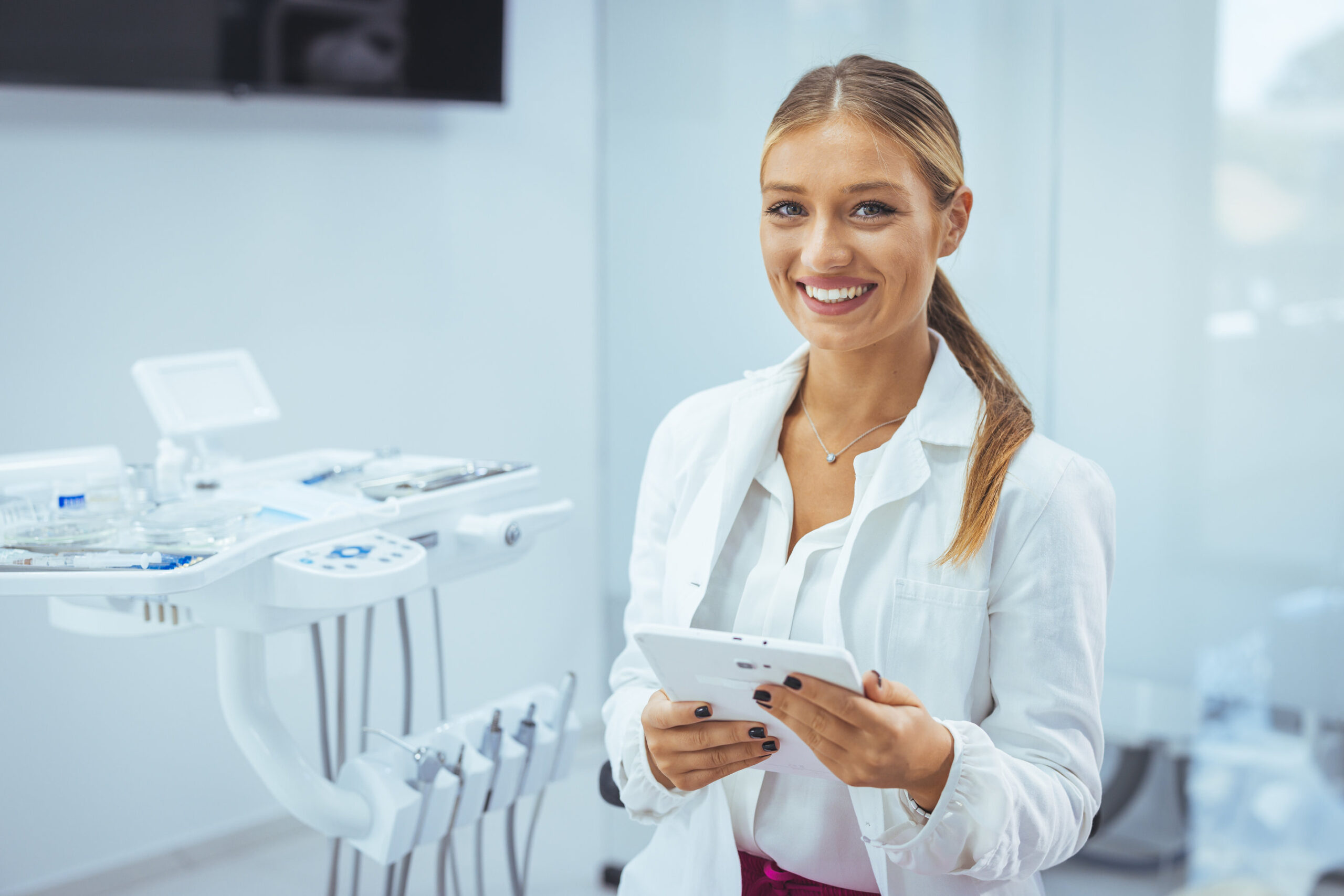 Portrait of a Caucasian woman dentist, sitting in her office next to a dentist chair, smiling. Portrait of female dentist. She standing at her office. Healthcare and medicine concept