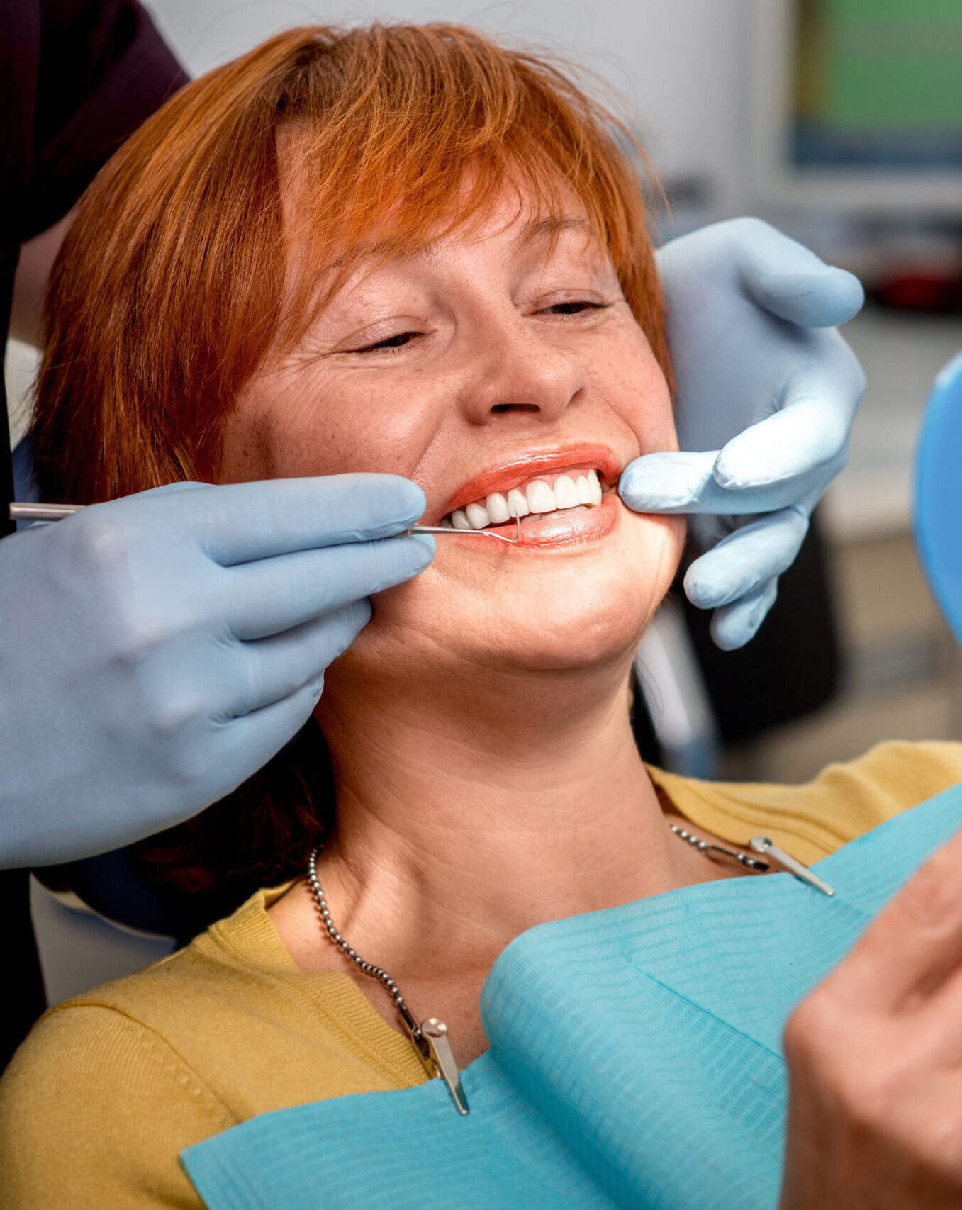 Smiling senior woman with new dental implants sitting in the dental office and looking at the mirror